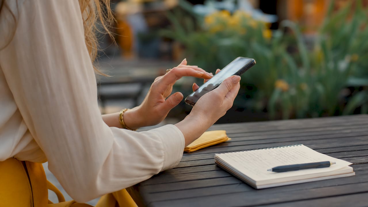Persona organizando estrategias de marketing digital con el móvil en una mano y tomando apuntes con la otra