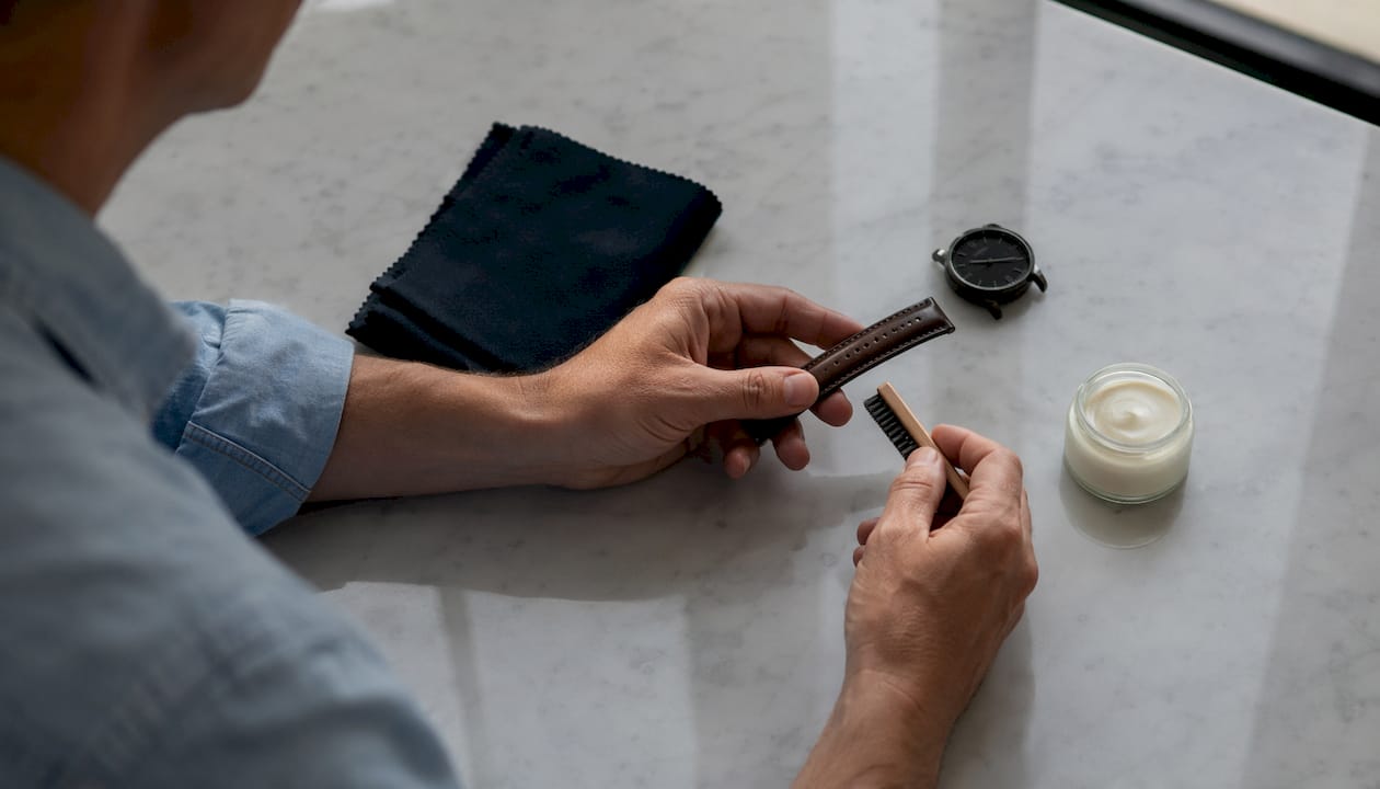 Hands conditioning leather watch strap at oak table