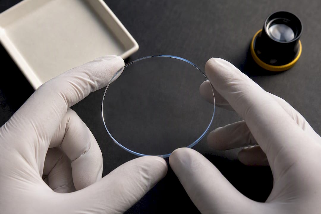 Gloved hand holding a synthetic sapphire wafer