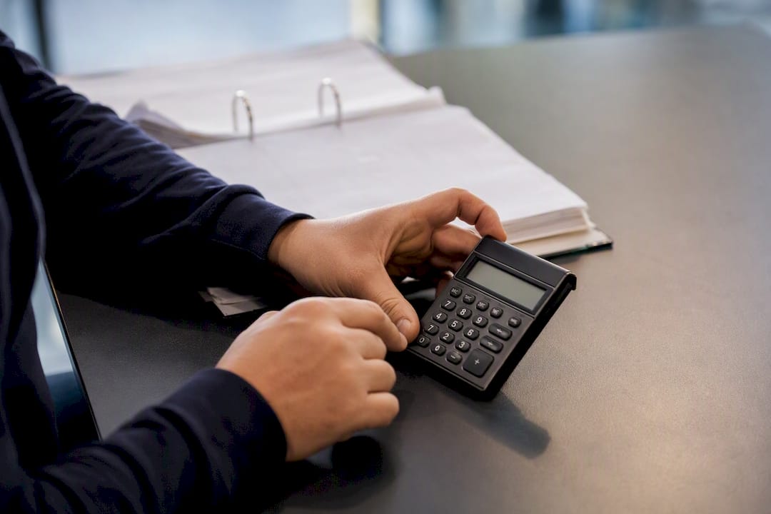 Handen die een rekenmachine gebruiken op een bureau met een kasboek