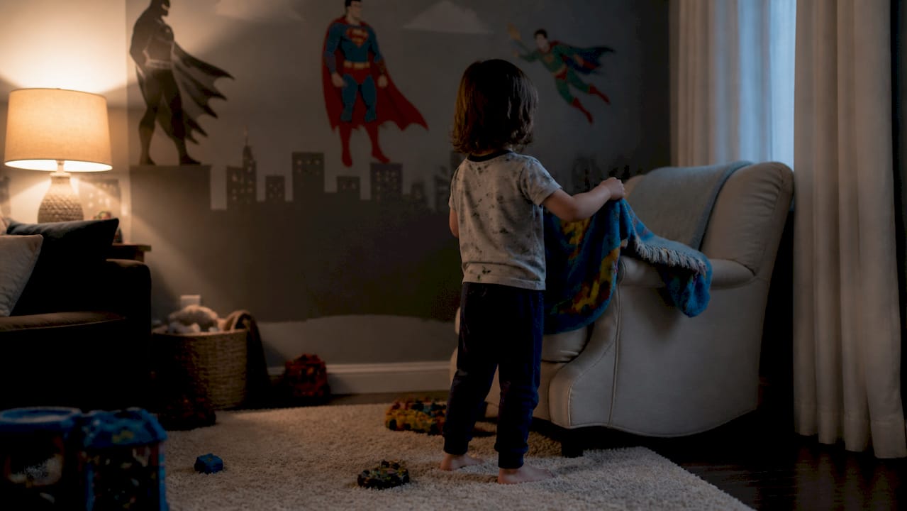Child hanging imaginary cape on bedpost
