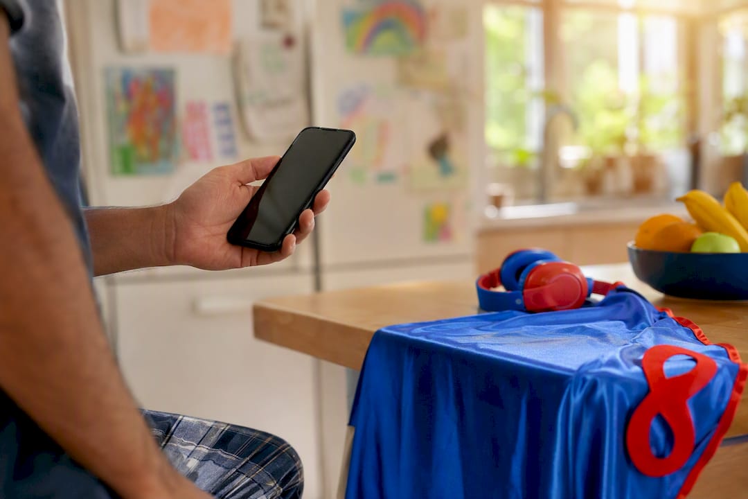 Parent holding smartphone near child's superhero cape