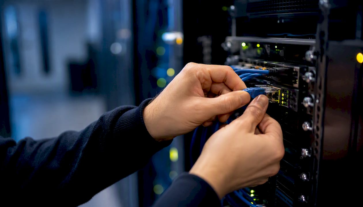 Une personne connecte un câble Ethernet dans une baie de serveurs.