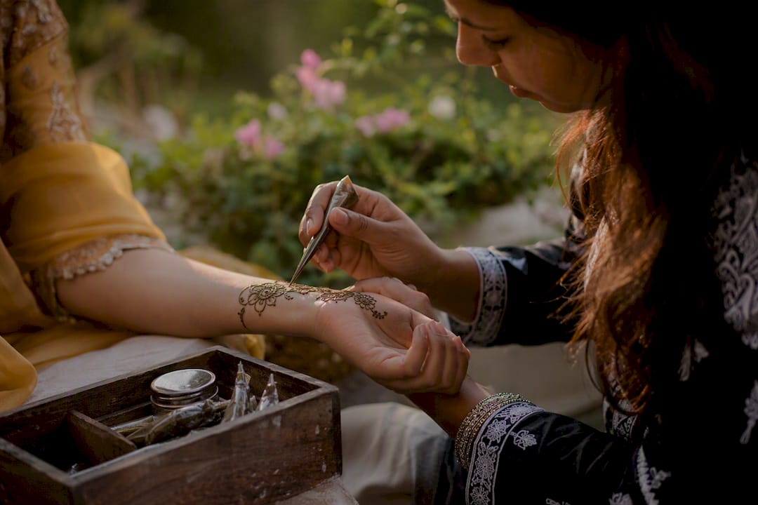 Henna artist applying floral henna design on arm
