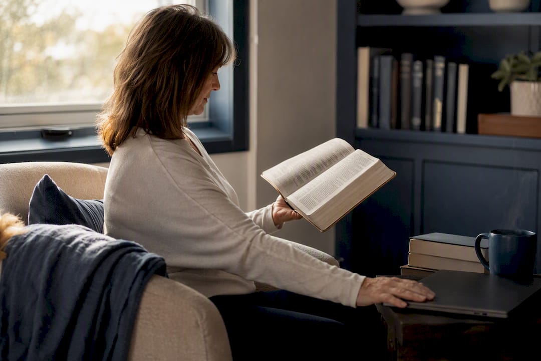 Person turning Bible page next to laptop