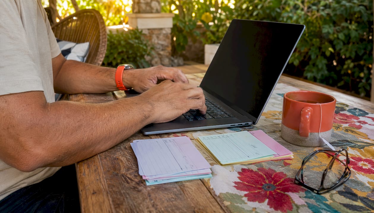 Hands typing on laptop with service scores paperwork