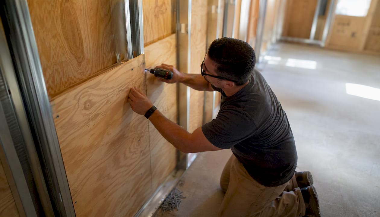 Hands fastening plywood backer to metal studs