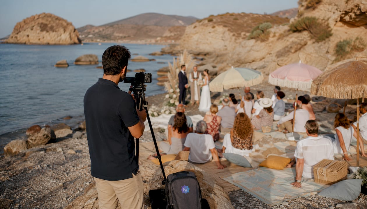 Videógrafo capturando los momentos de una boda en la playa durante la ceremonia.