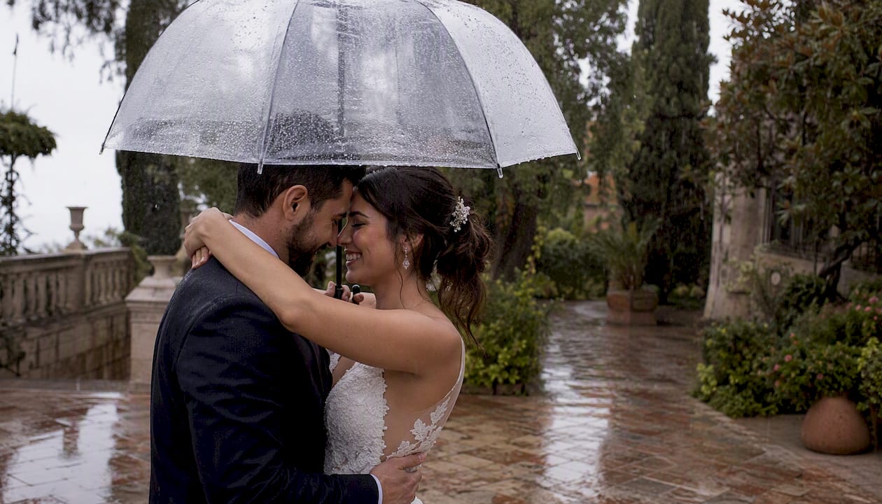 Una pareja se abraza bajo un paraguas transparente mientras llueve.