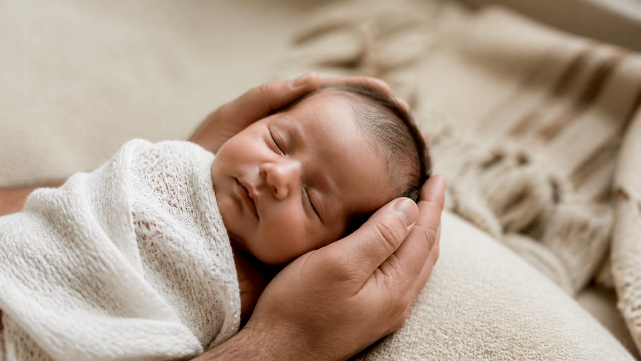 Recién nacido durmiendo plácidamente entre las manos de sus padres