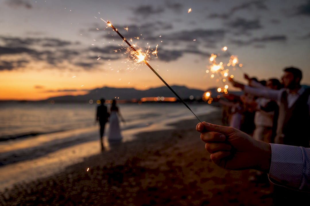 Manos sosteniendo bengalas de boda encendidas al atardecer