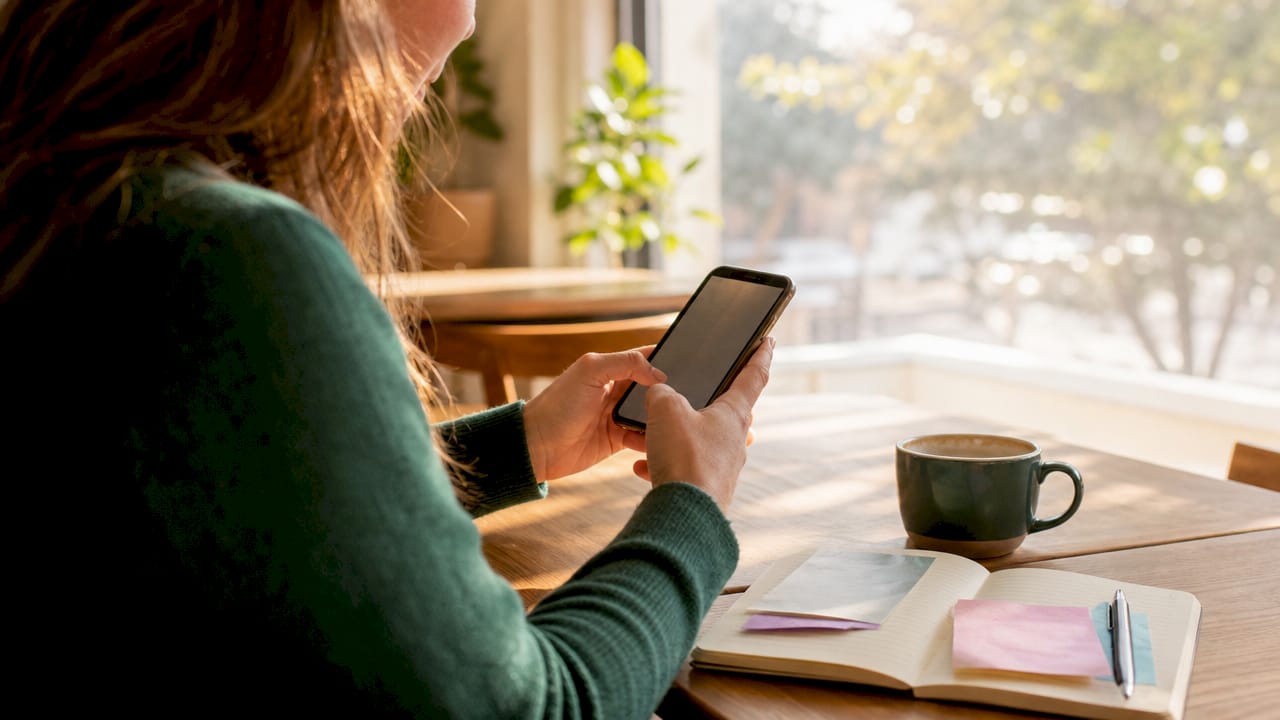Hands holding smartphone reading reviews on wooden desk