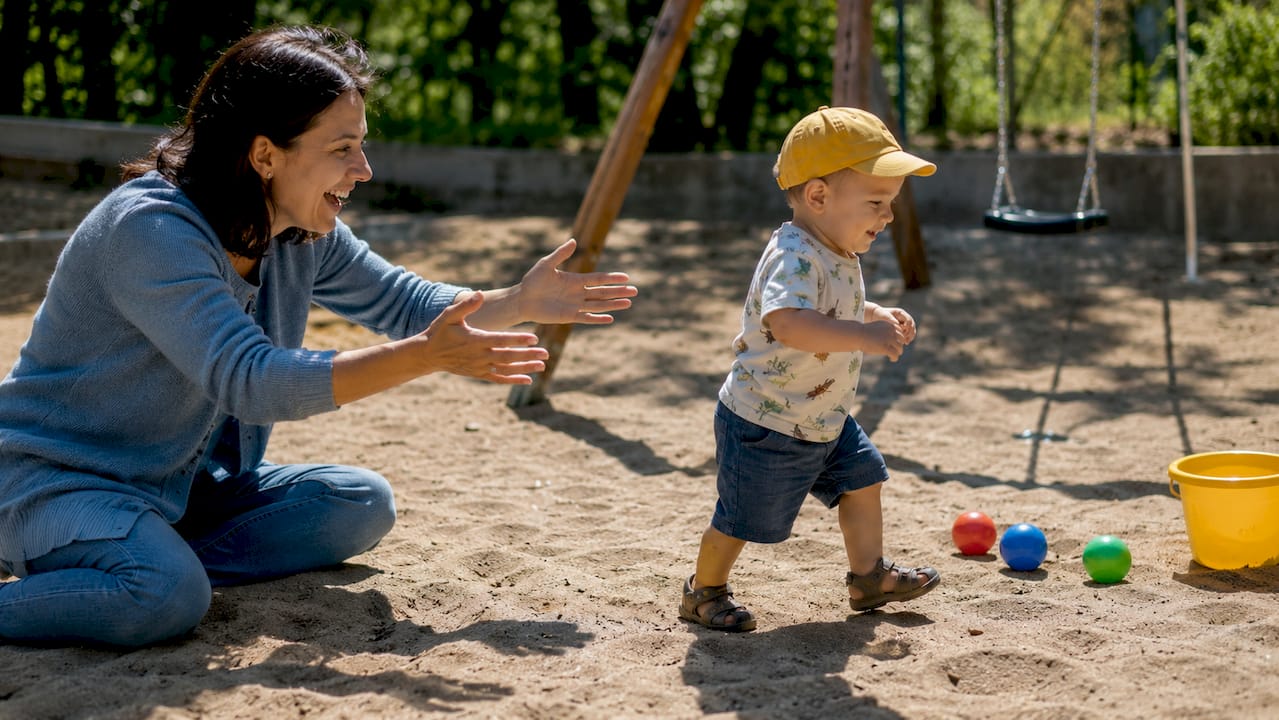 Mother encouraging toddler walking outdoors