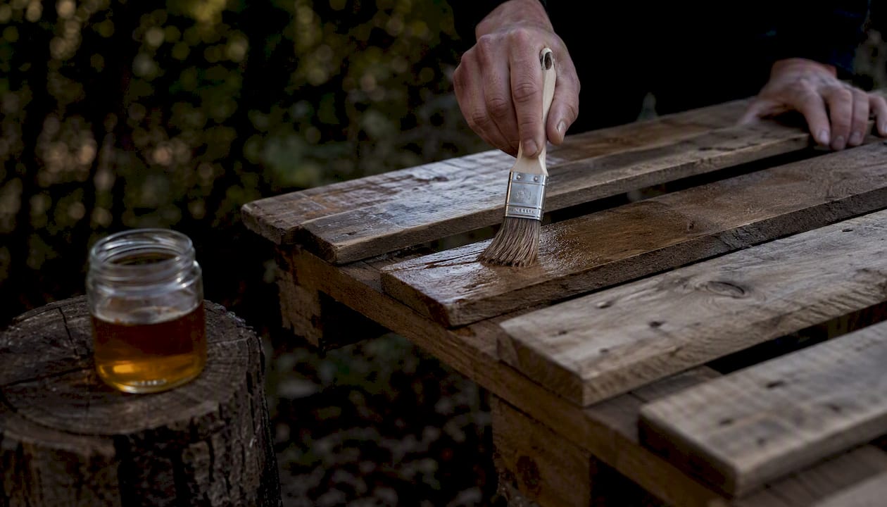 On applique de l’huile à la main sur des palettes en bois, à l’extérieur, pour les protéger et leur redonner de l’éclat.