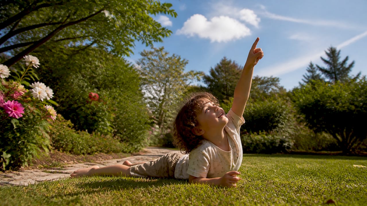 Child pointing at clouds lying in grass