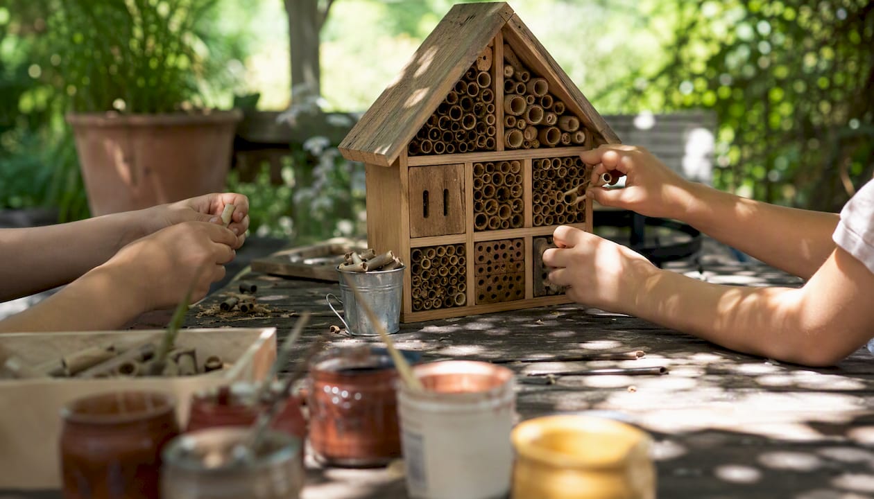 Des enfants s’amusent à remplir les petits compartiments d’un hôtel à insectes lors d’une activité en plein air.