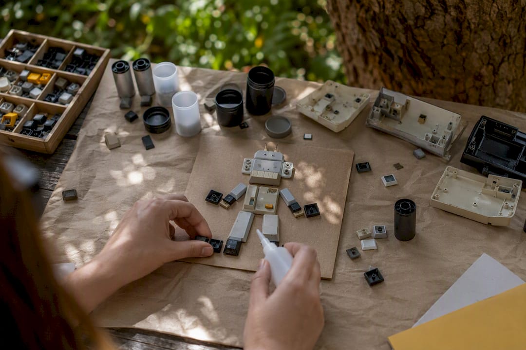 Hands gluing keyboard keys for recycled robot collage
