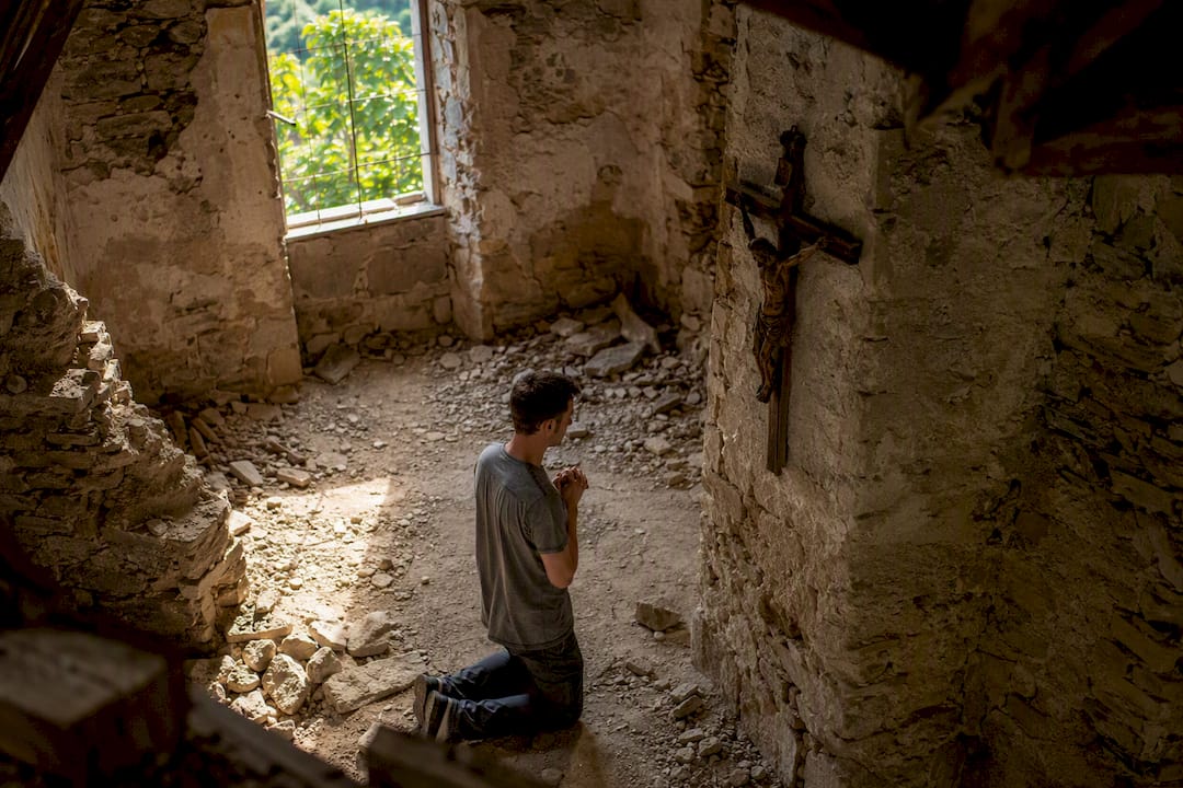 Man kneeling in prayer in ruined chapel