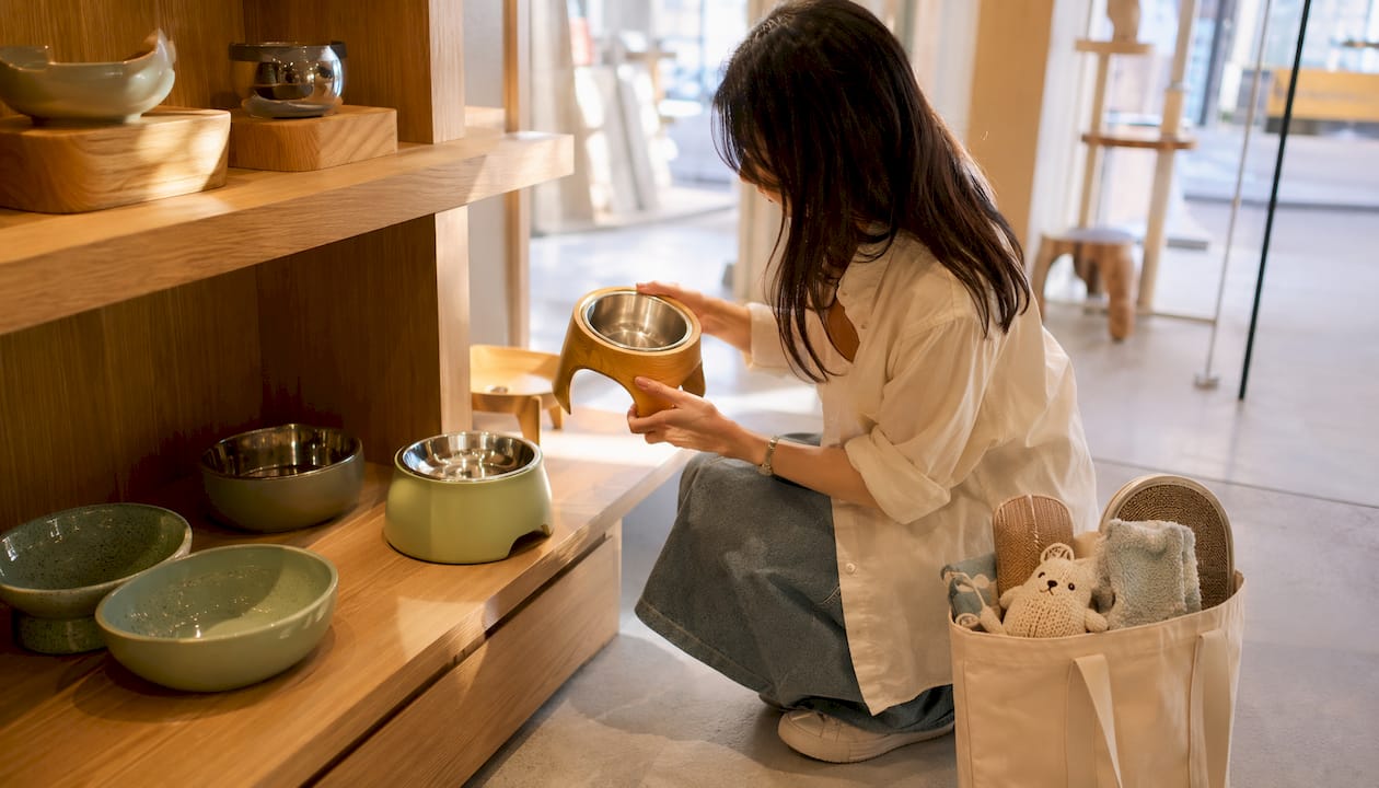 Woman selecting elevated cat bowls in pet store aisle