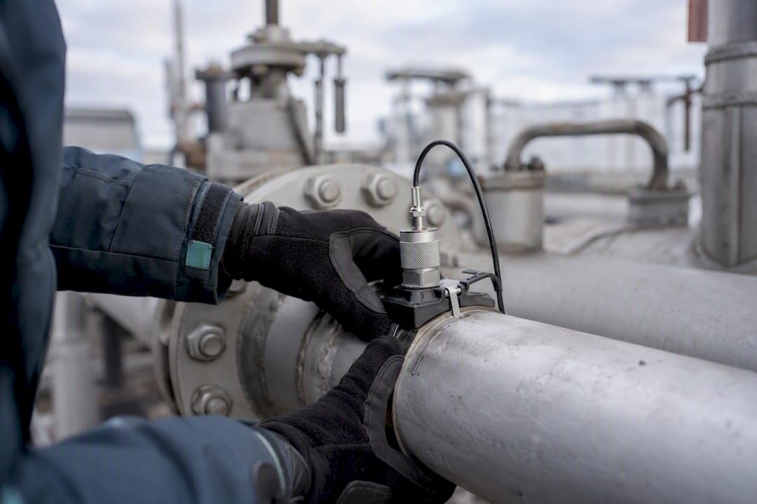 Hands installing acoustic sensor on pipeline