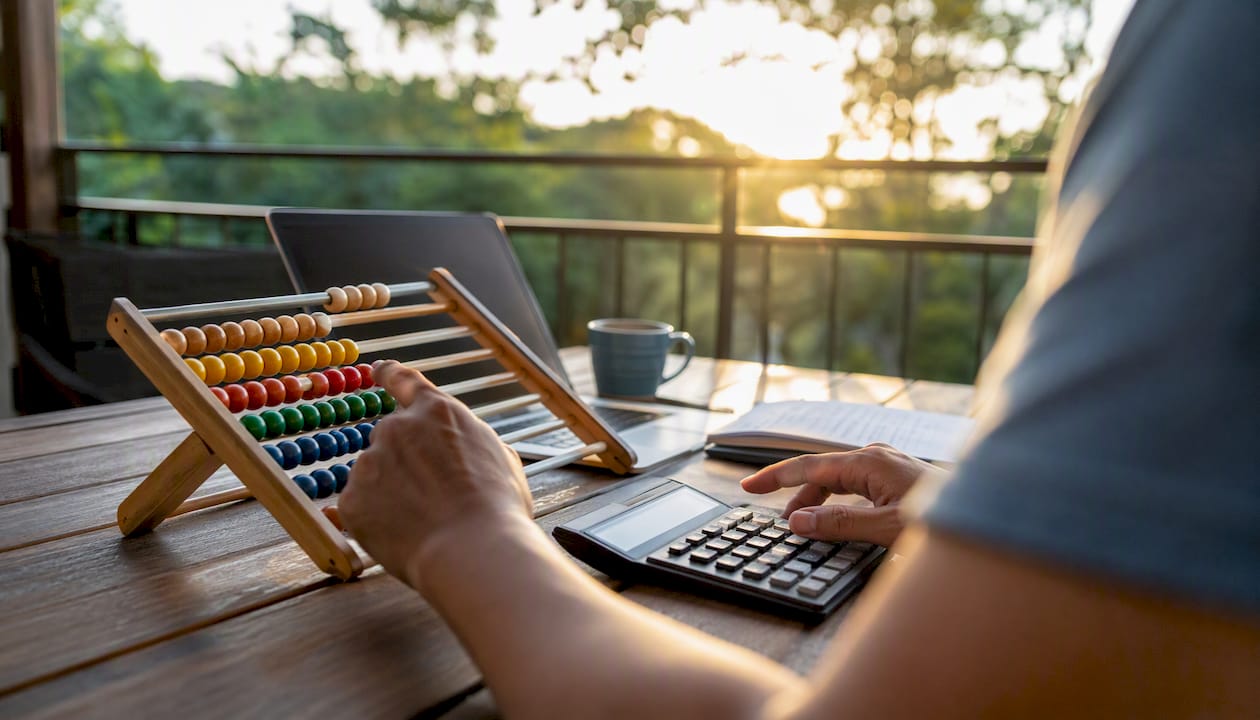 Hands adjusting abacus with calculator on desk