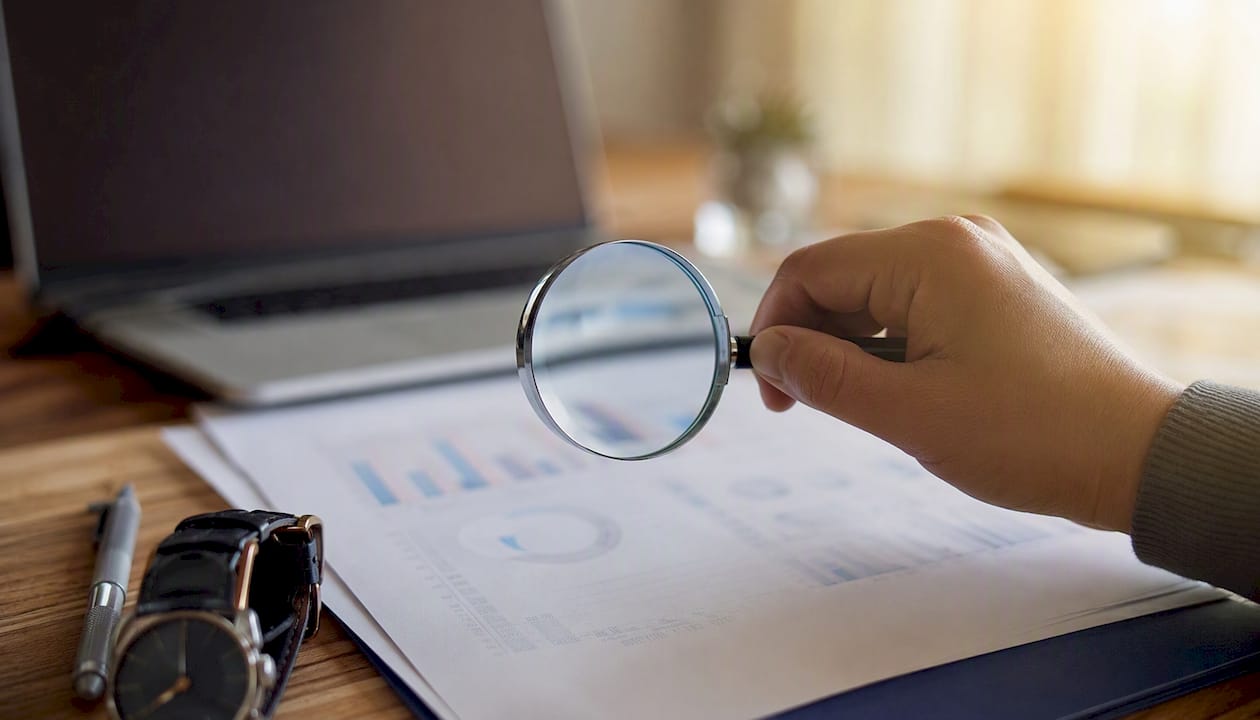 Hand holding magnifying glass over research charts
