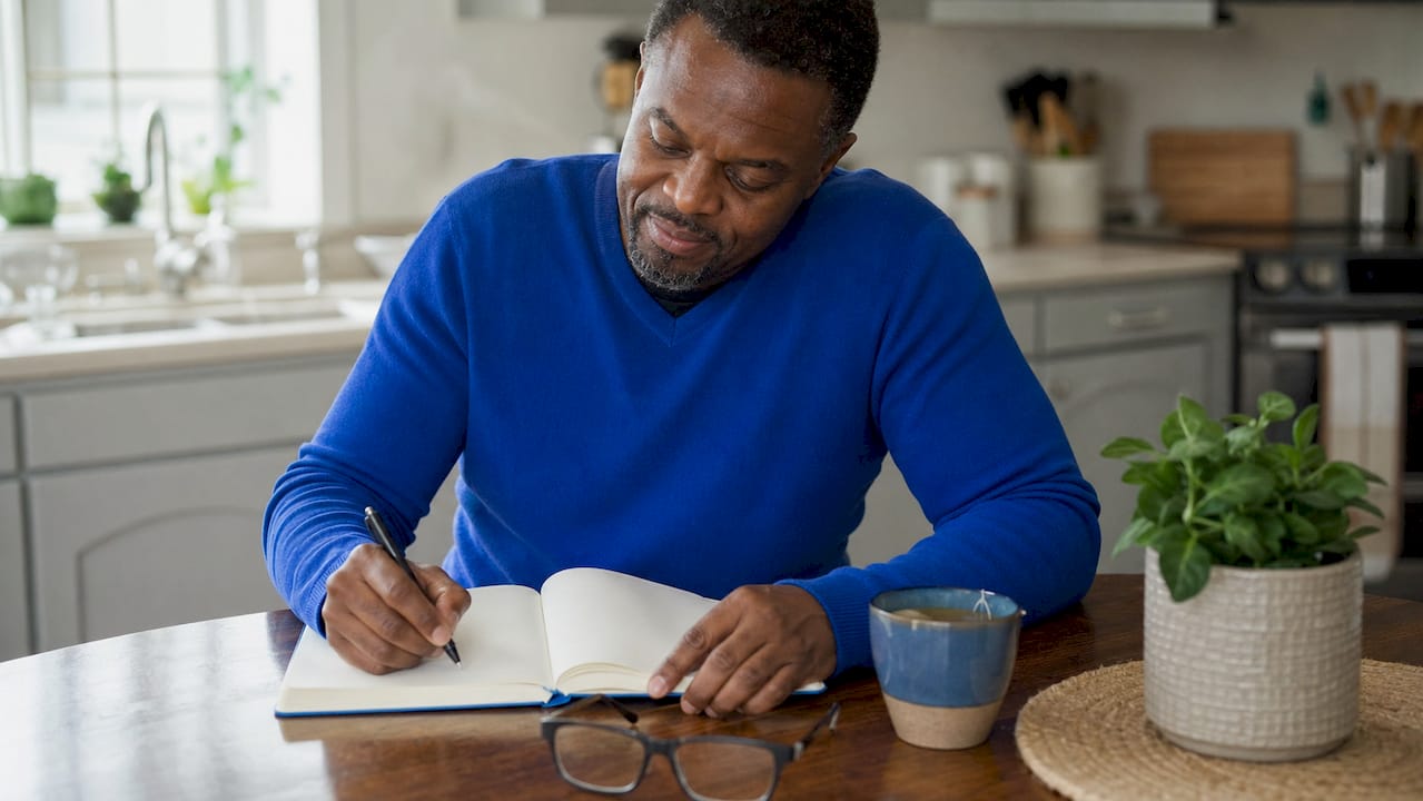 Man writing workplace stress log in notebook