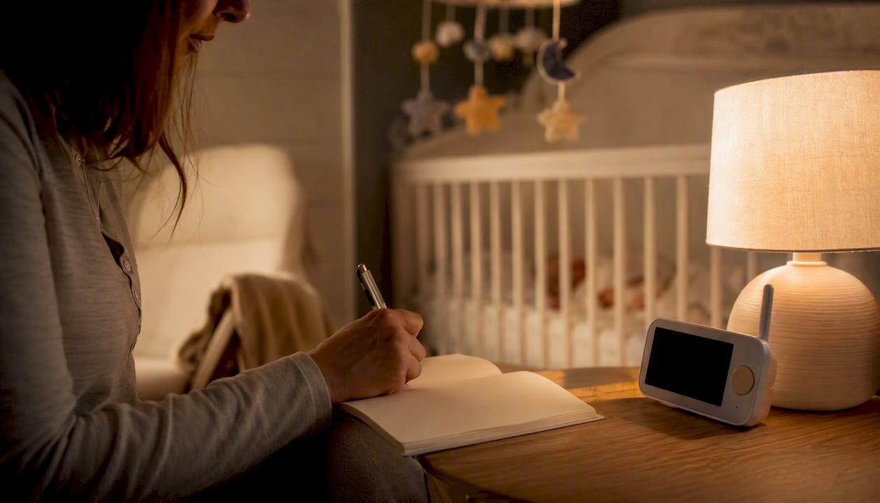 Parent recording sleep log by bedside lamp