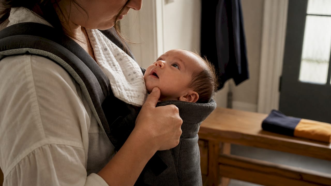 Caregiver checking newborn airway in carrier