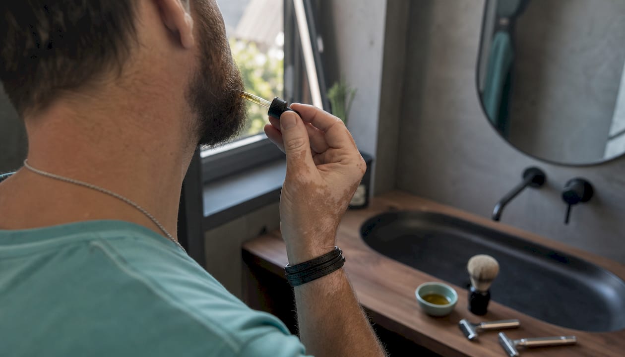 Detailný záber na ruku, ktorá nanáša olej na bradu