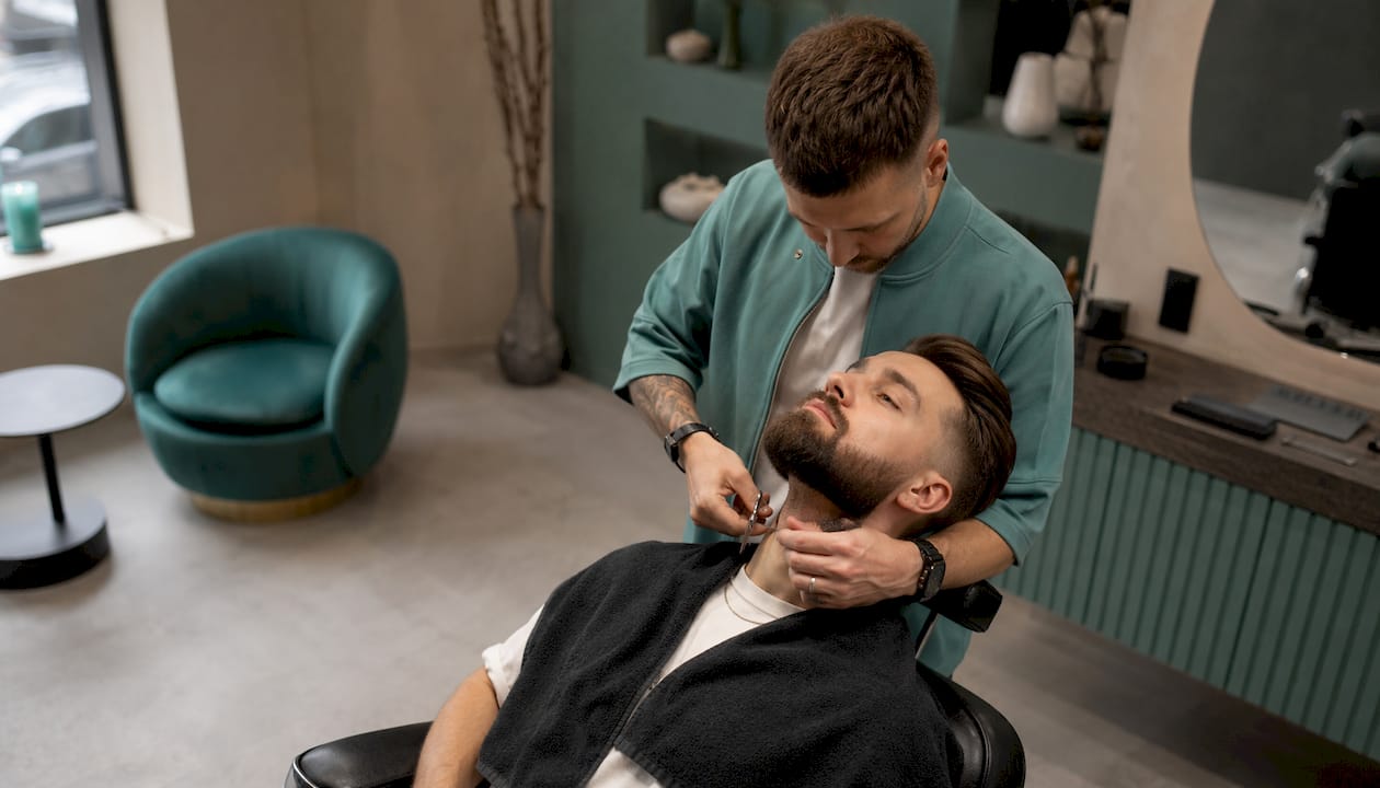 Barber precízne upravuje bradu zákazníkovi do moderného prechodu.