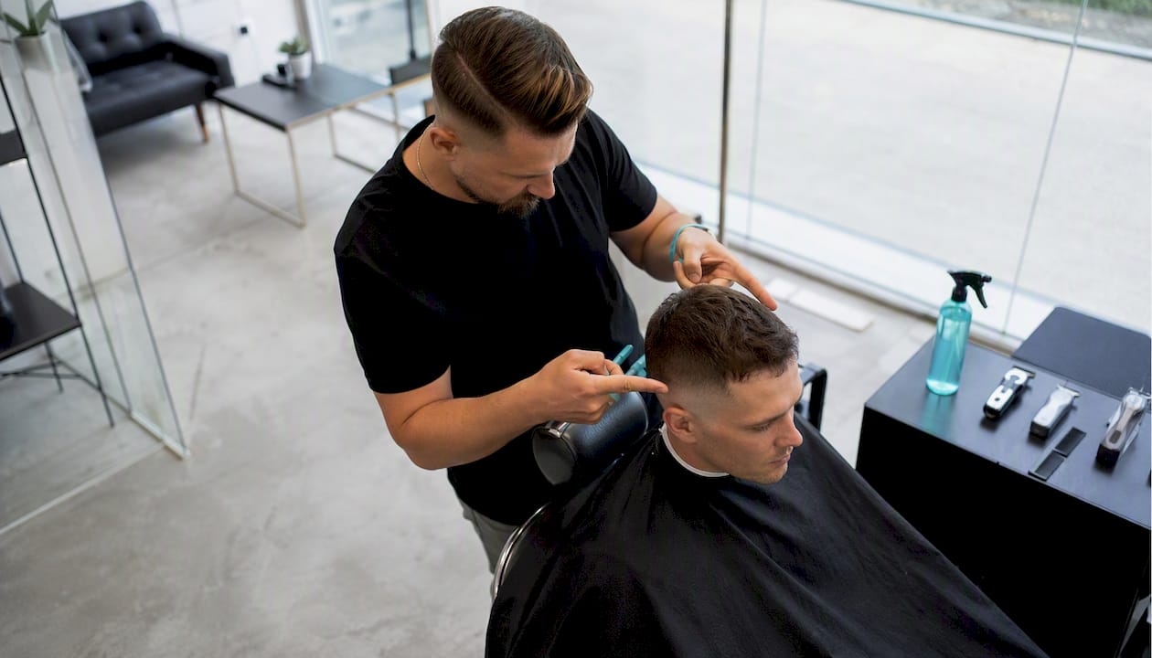 Kaderník vysvetľuje zákazníkovi, ako vyzerá strih s postupným prechodom dohola (high fade) a čo od neho môže očakávať.