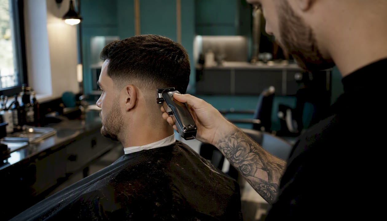 Barber práve upravuje boky účesu s nízkym prechodom.