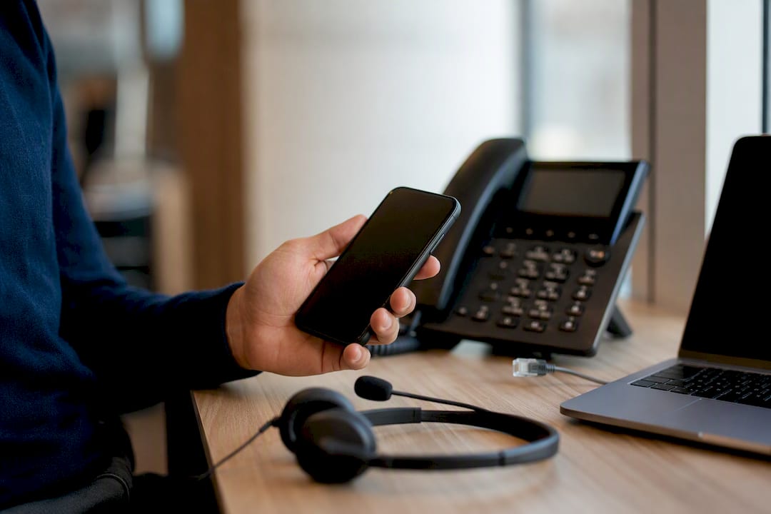 Hand met smartphone geïntegreerd in het kantoortelefoonsysteem