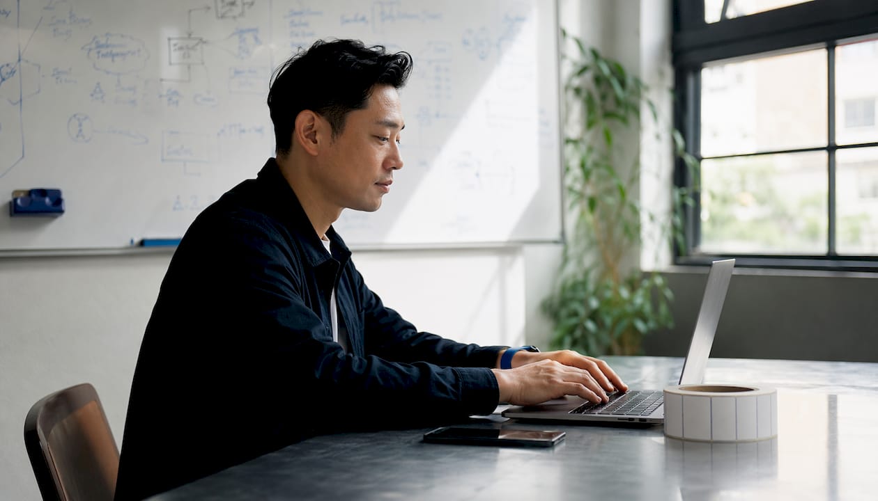 Des mains s’activent sur un clavier, à côté de piles d’étiquettes prêtes à être expédiées.