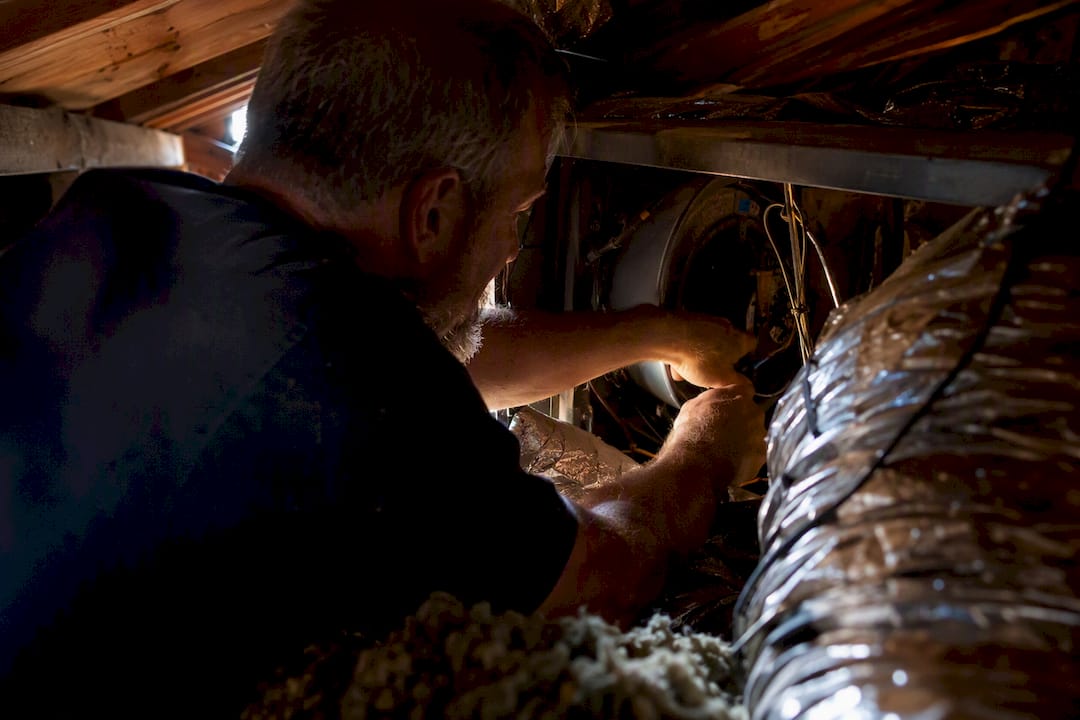 Hands working on blower motor in attic space