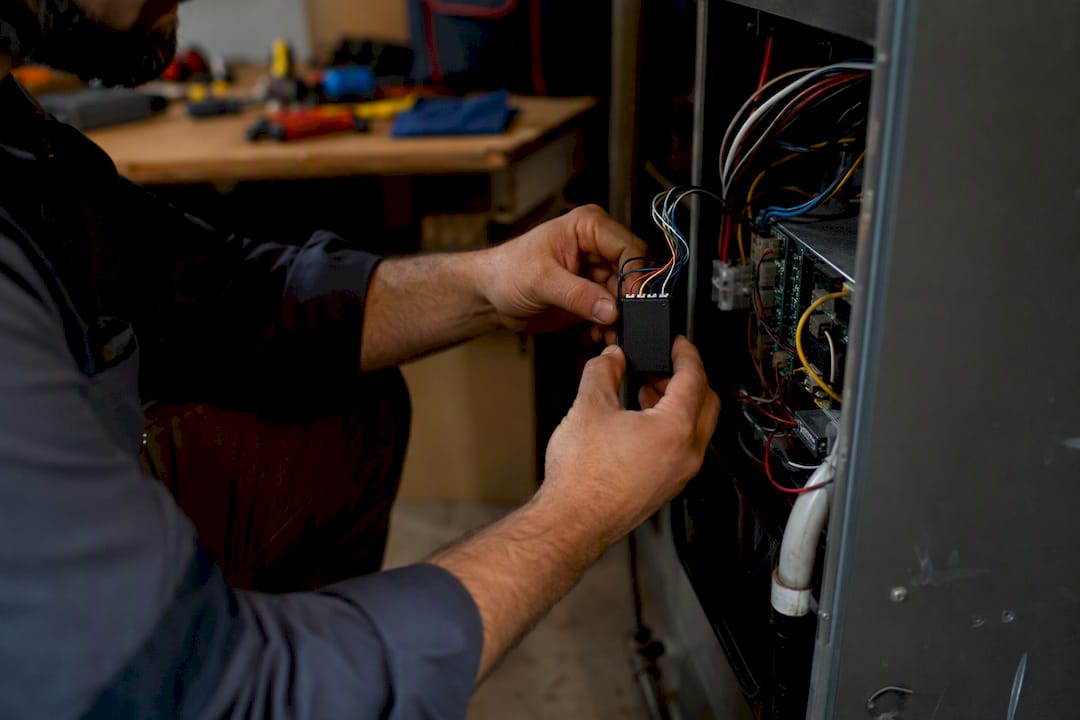 Hands installing C-wire adapter near furnace