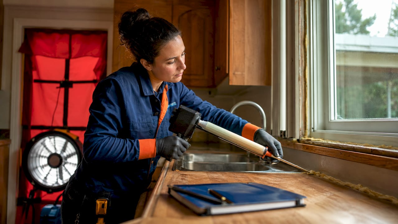 Hands sealing window frame during home envelope upgrade