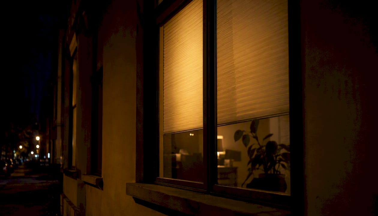 Durch das Fenster fällt in der Nacht helles Licht aus einem Zimmer nach draußen.
