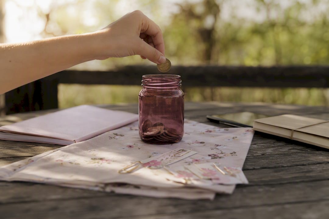 Hands dropping coins into jar on table