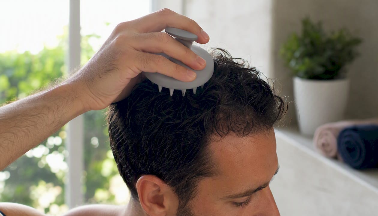 Hand using silicone scalp brush on scalp