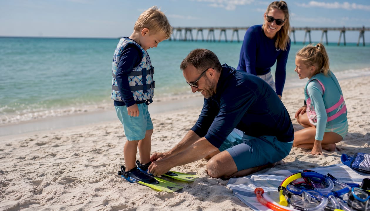Parent fitting full-foot fins on child for snorkeling