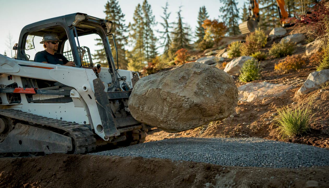 Contractor moving large boulder with skid steer