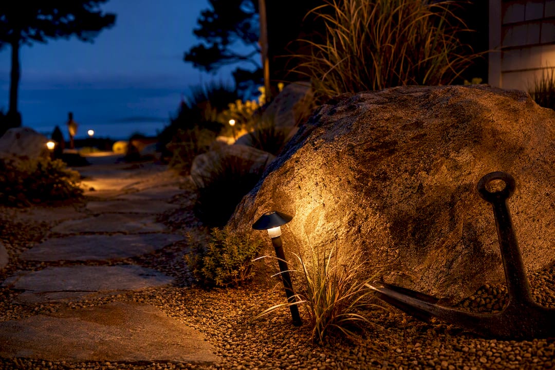 Warm path light illuminating coastal garden boulder