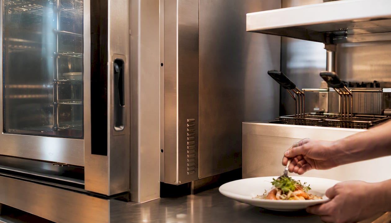 Commercial oven with heat shield near fryer in kitchen