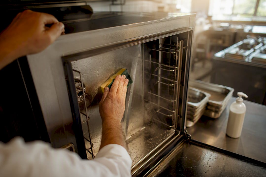 Hands wiping inside combi oven chamber