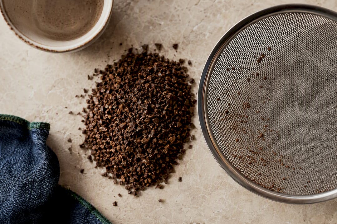 Coarse coffee grounds beside mesh filter