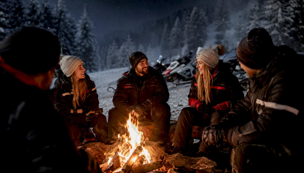 Riders warming hands at bonfire during night snowmobile tour