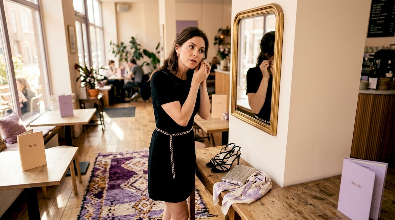 Woman styling little black dress with accessories in apartment