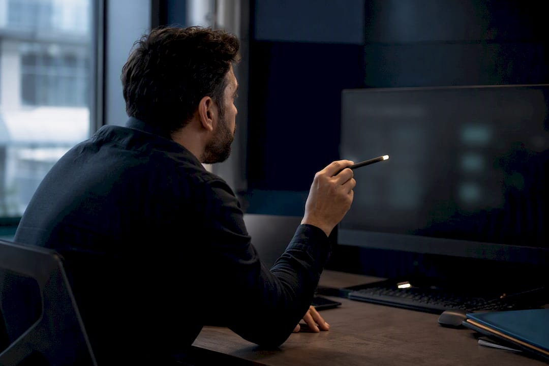 Hand pointing with pen at blurred screen in tech workspace